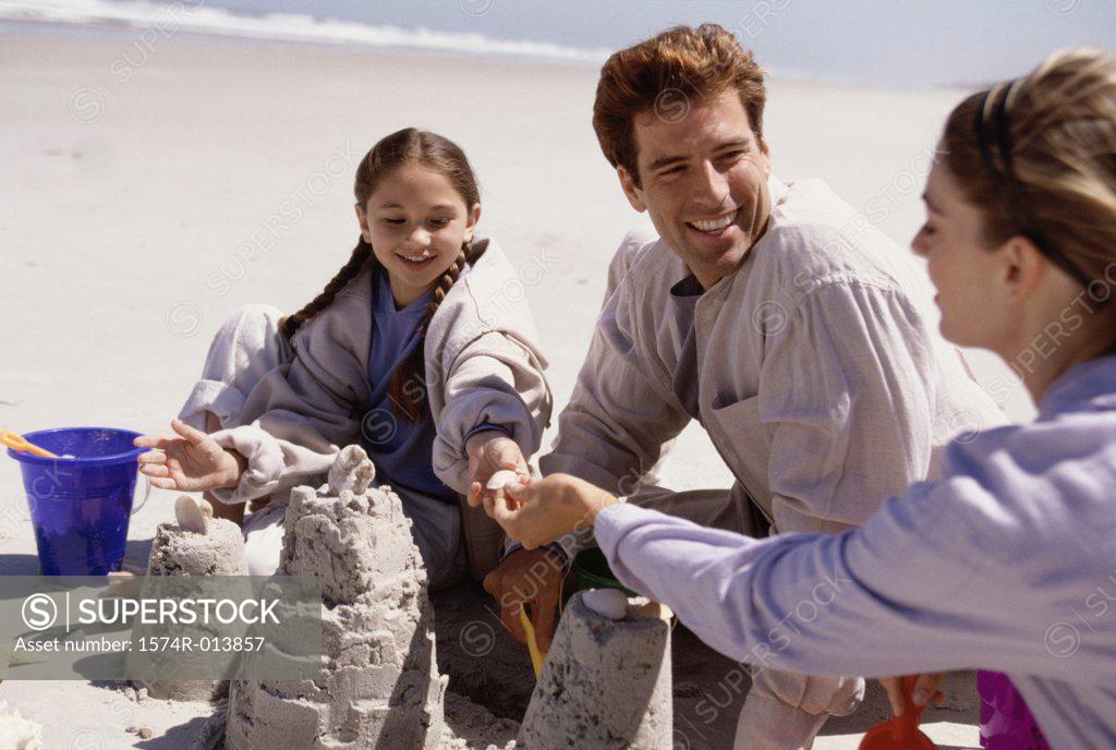Stock Photo: 1574R-013857 Parents and their daughter making a sand castle on the beach