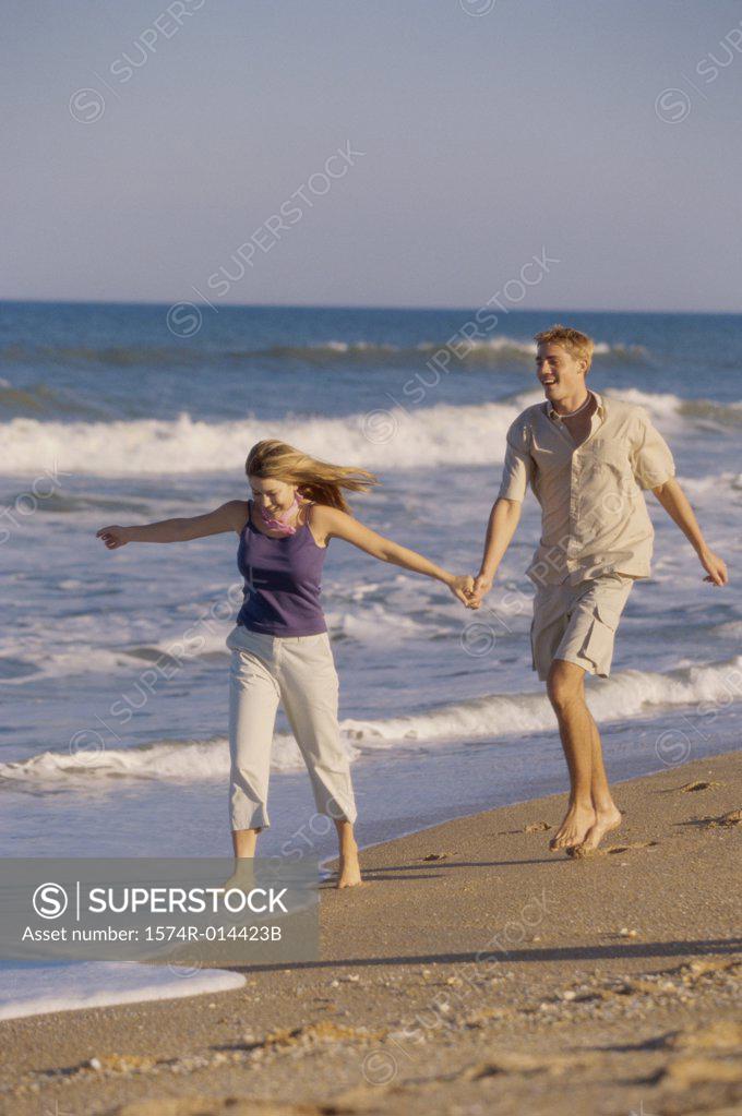 Stock Photo: 1574R-014423B Young man and a teenage girl running on the beach