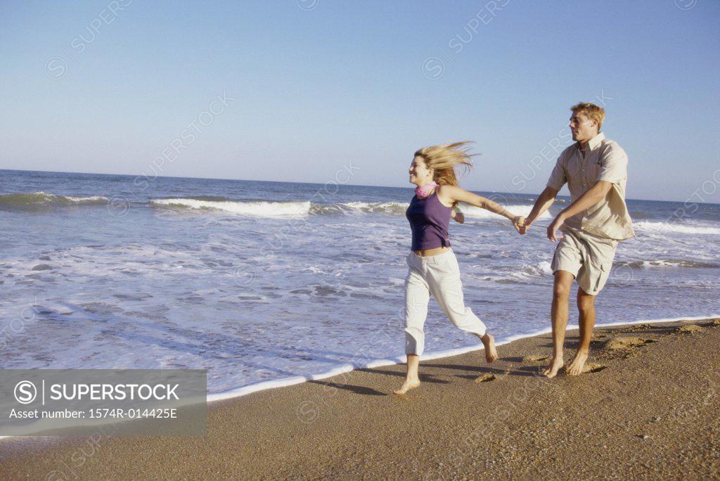 Stock Photo: 1574R-014425E Teenage girl running with a young man on the beach