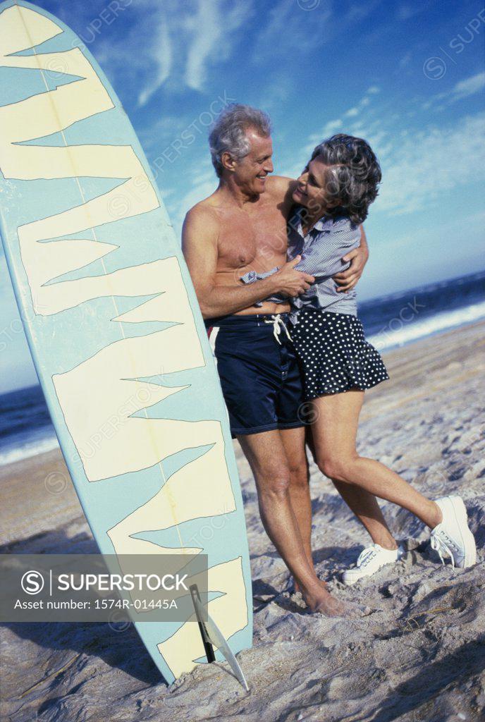 Stock Photo: 1574R-01445A Senior couple at the beach near a surfboard