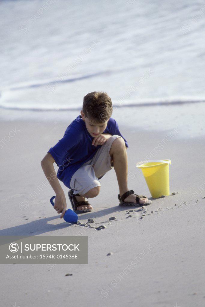 Stock Photo: 1574R-014536E Boy digging sand with a shovel on the beach