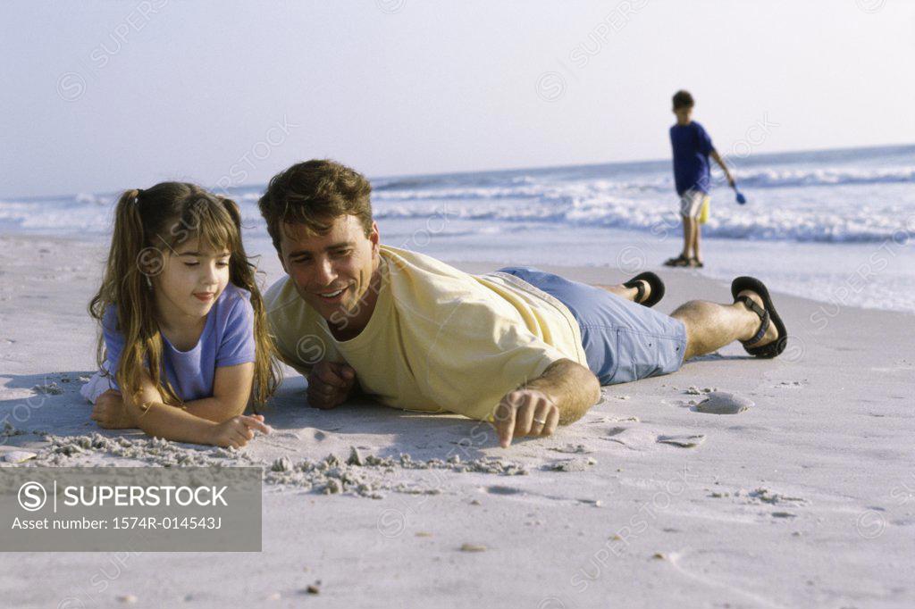 Stock Photo: 1574R-014543J Father and his daughter writing in sand on the beach