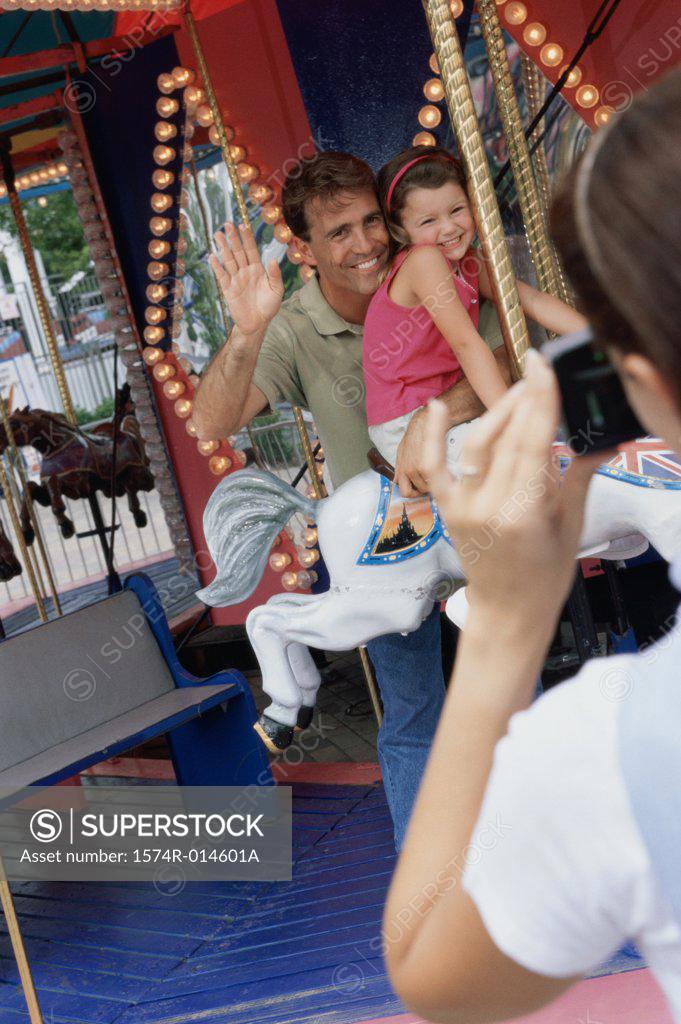 Stock Photo: 1574R-014601A Rear view of a woman taking a photograph of her husband and daughter sitting on a carousel horse