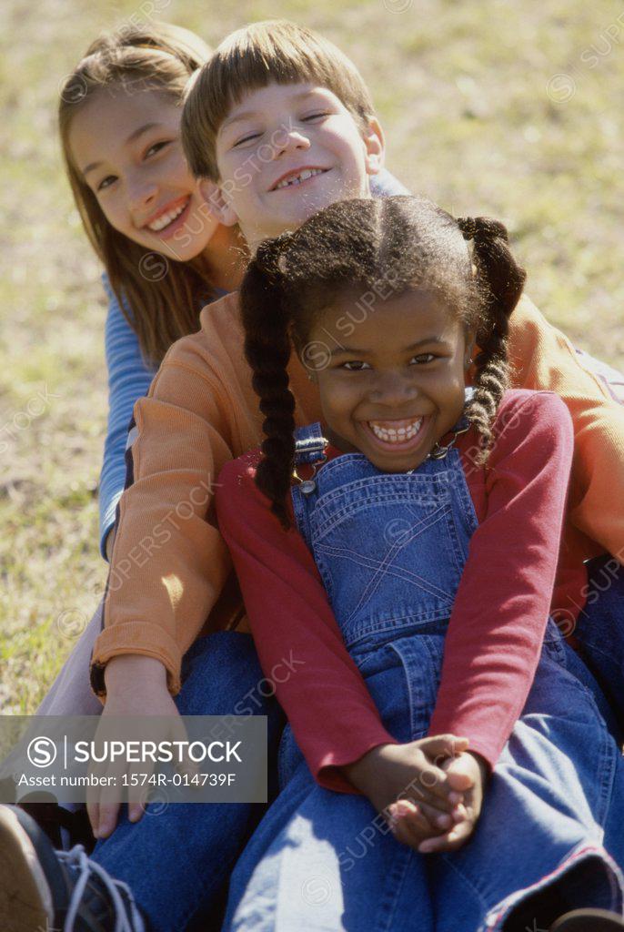 Stock Photo: 1574R-014739F Portrait of two girls and a boy sitting on a lawn