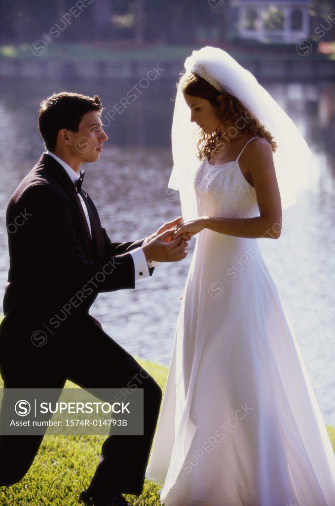 Stock Photo: 1574R-014793B Side profile of a groom proposing to his bride near a lake