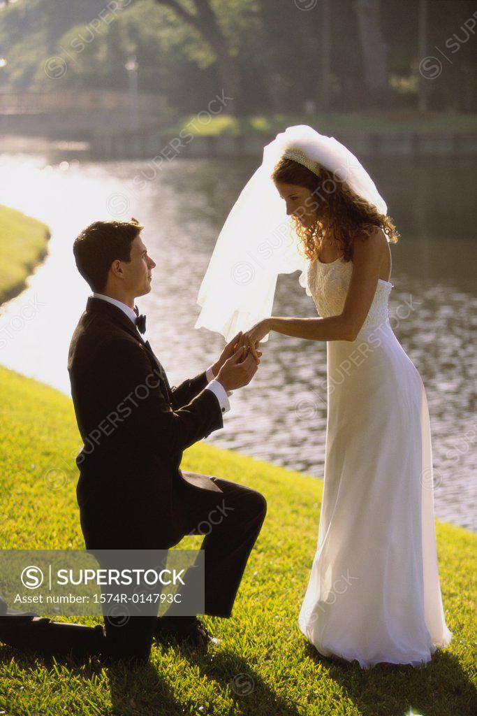 Stock Photo: 1574R-014793C Side profile of a groom proposing to his bride near a lake