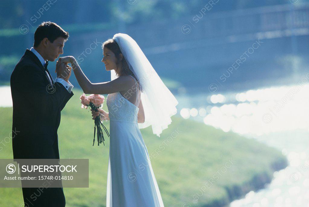 Stock Photo: 1574R-014810 Side profile of a groom kissing his bride's hand near a lake