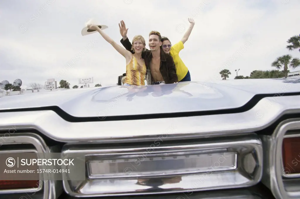 Young man and two young women waving in a convertible car
