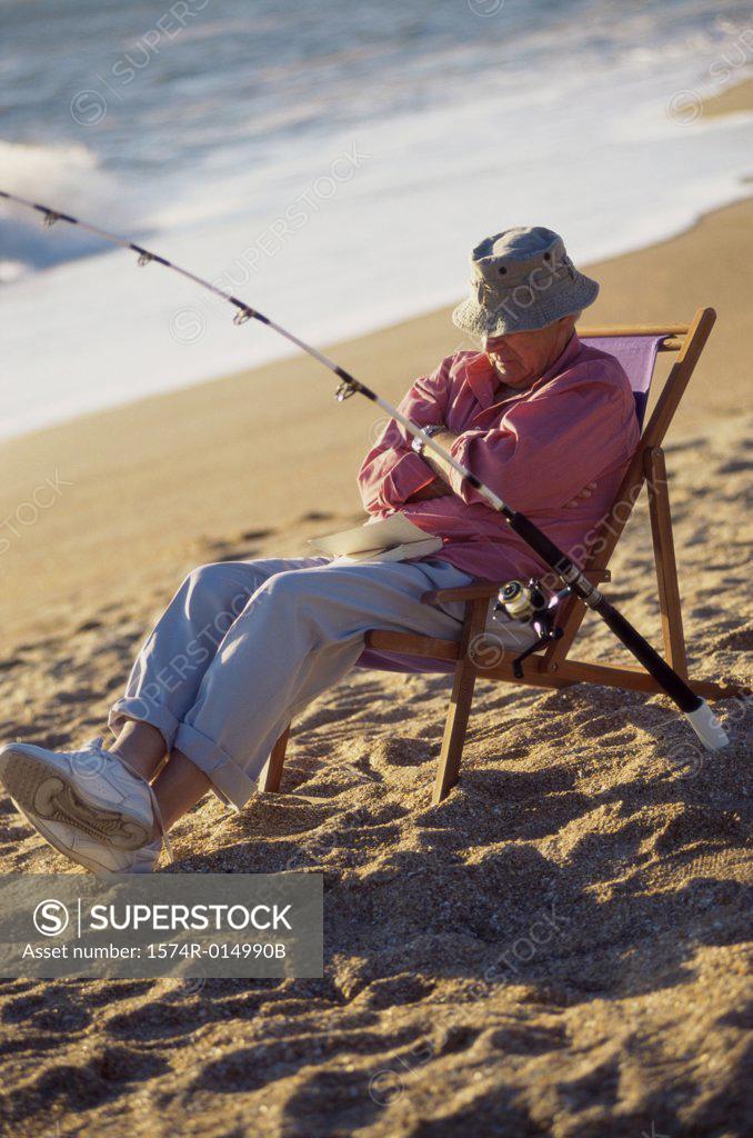 Stock Photo: 1574R-014990B Senior man sitting on the beach in a deck chair with a fishing rod
