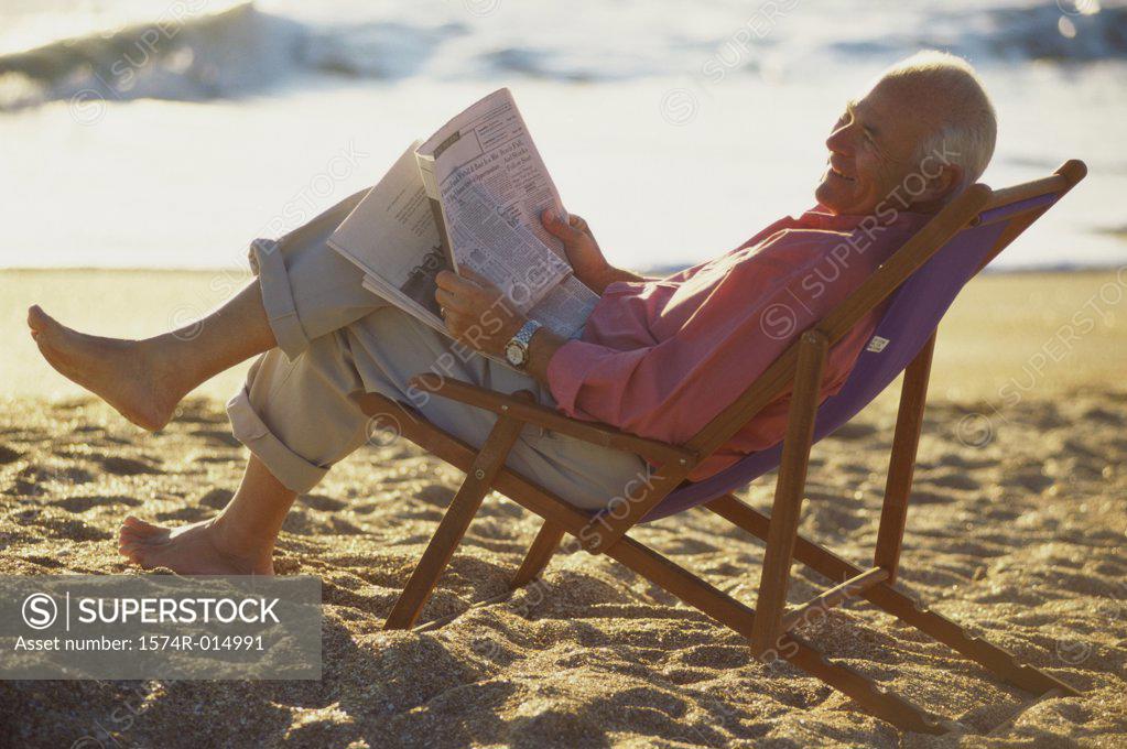 Stock Photo: 1574R-014991 Side profile of a senior man reading a newspaper on the beach