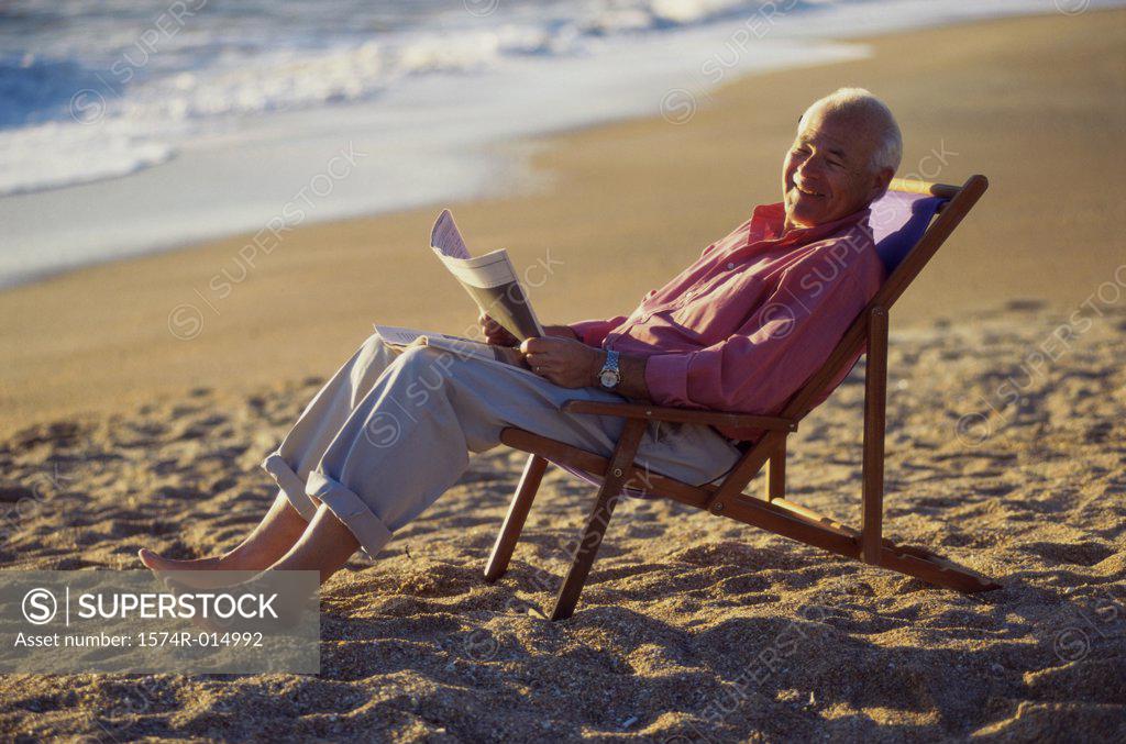 Stock Photo: 1574R-014992 Side profile of a senior man holding a newspaper on the beach