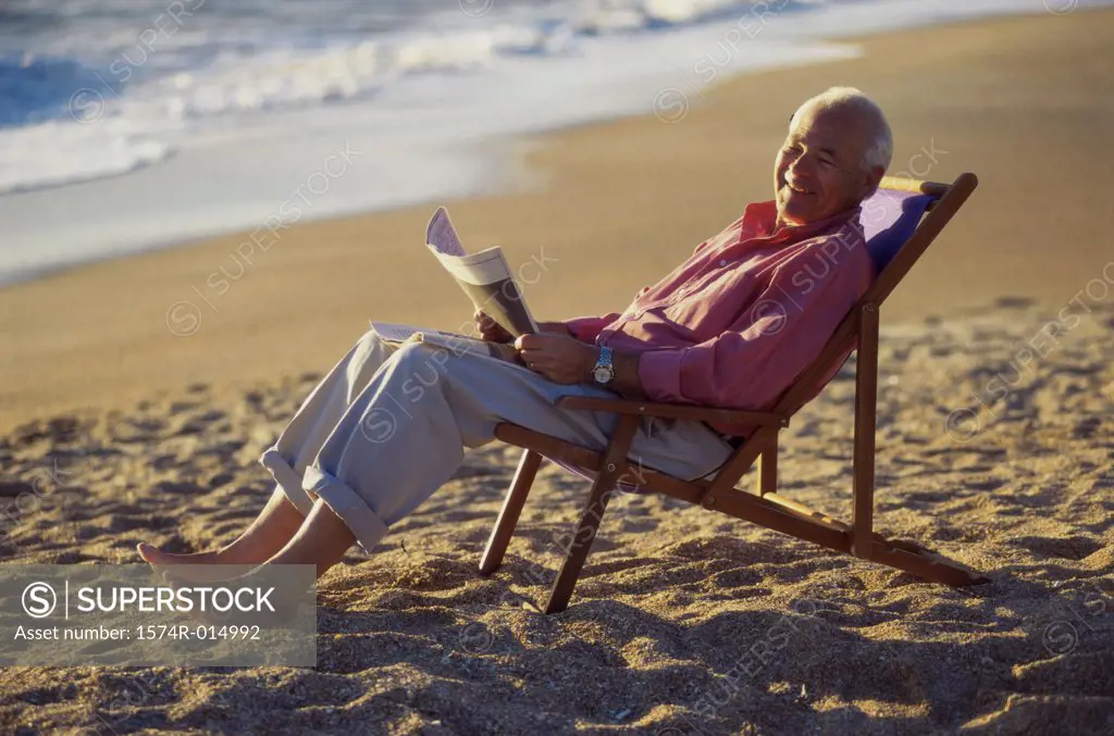 Side profile of a senior man holding a newspaper on the beach