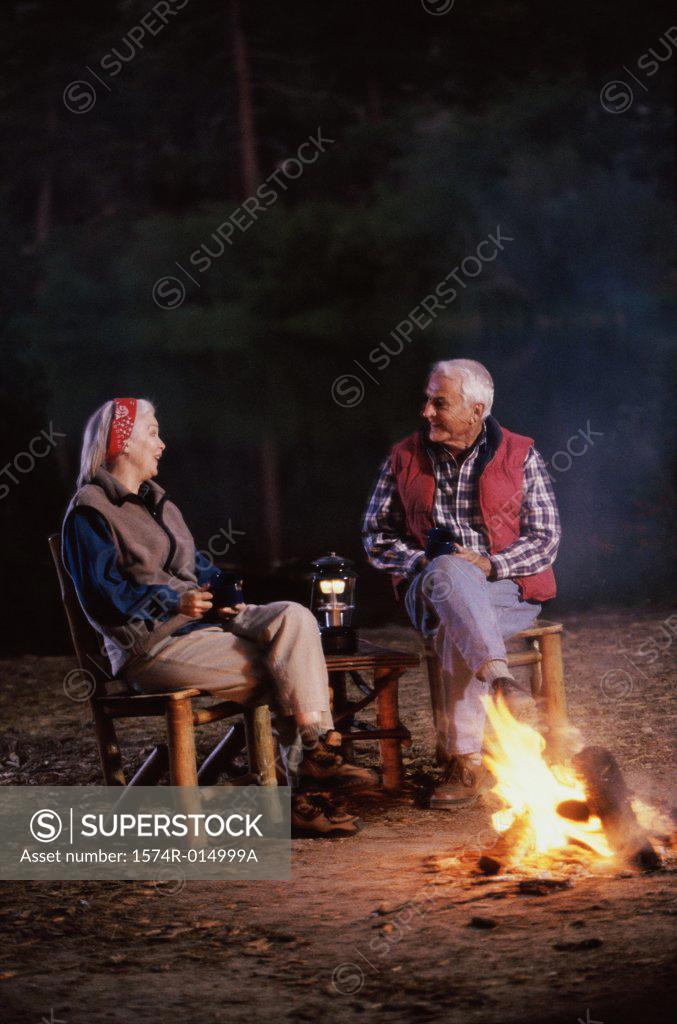 Stock Photo: 1574R-014999A Senior couple sitting near a campfire talking to each other