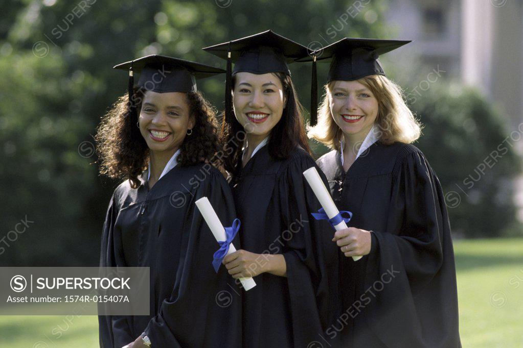 Stock Photo: 1574R-015407A Three young women wearing graduation gowns and holding diplomas