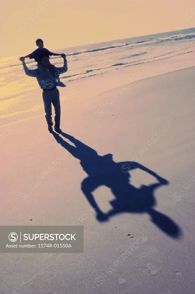 Silhouette of a man carrying his son on his shoulders at the beach