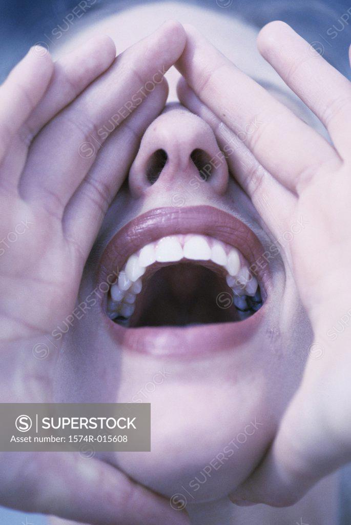 Stock Photo: 1574R-015608 Close-up of a young woman with her hands over her mouth shouting