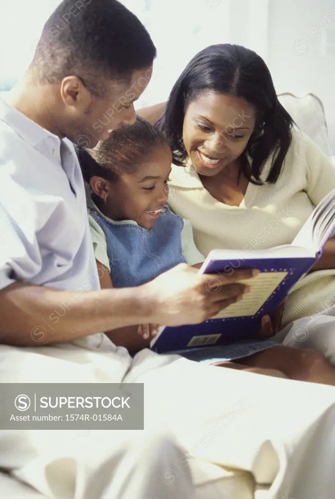 Parents and their daughter sitting together on a couch reading a book