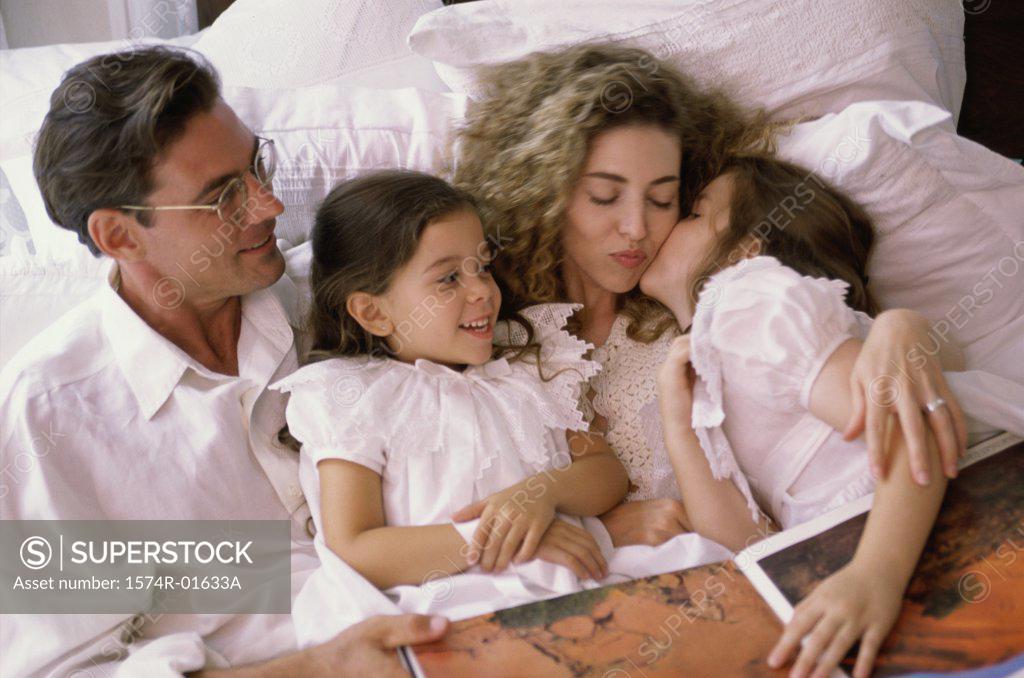 Stock Photo: 1574R-01633A Father and mother lying in bed with their two daughters