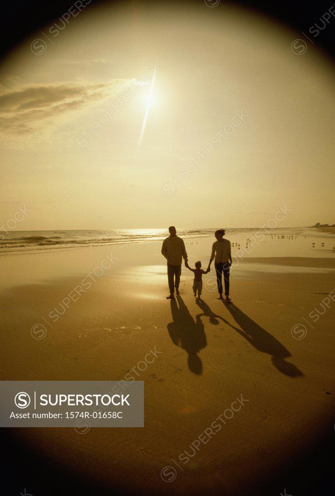 Stock Photo: 1574R-01658C Silhouette of a father and a mother with their daughter at the beach