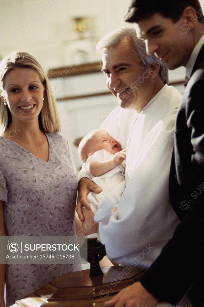 Stock Photo: 1574R-01673B Young couple standing with a priest carrying their baby
