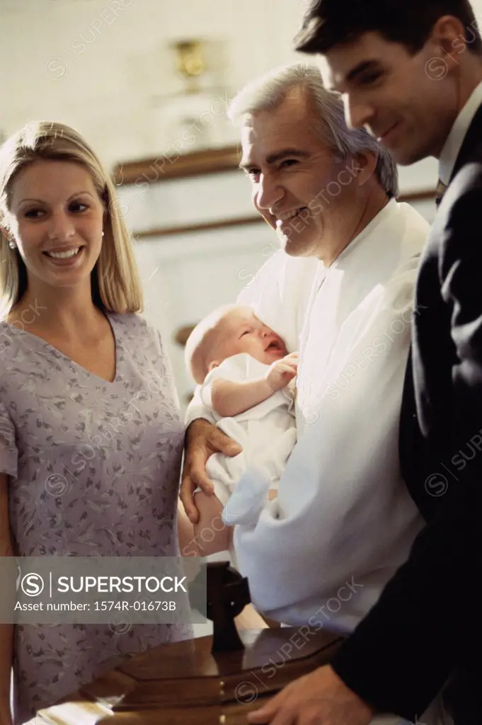 Young couple standing with a priest carrying their baby