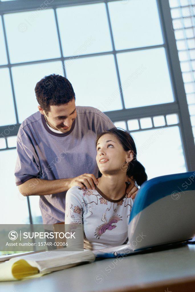 Stock Photo: 1574R-02086 Teenage girl sitting in front of a laptop with a teenage boy behind her