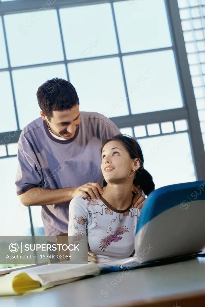 Teenage girl sitting in front of a laptop with a teenage boy behind her