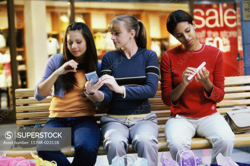 Stock Photo: 1574R-02311B Three teenage girls sitting on a bench in a shopping mall applying make-up