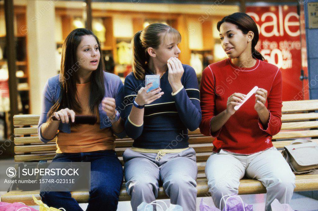 Stock Photo: 1574R-02311E Three teenage girls sitting on a bench in a shopping mall applying make-up