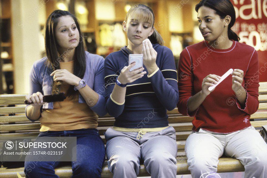 Stock Photo: 1574R-02311F Three teenage girls sitting on a bench in a shopping mall applying make-up