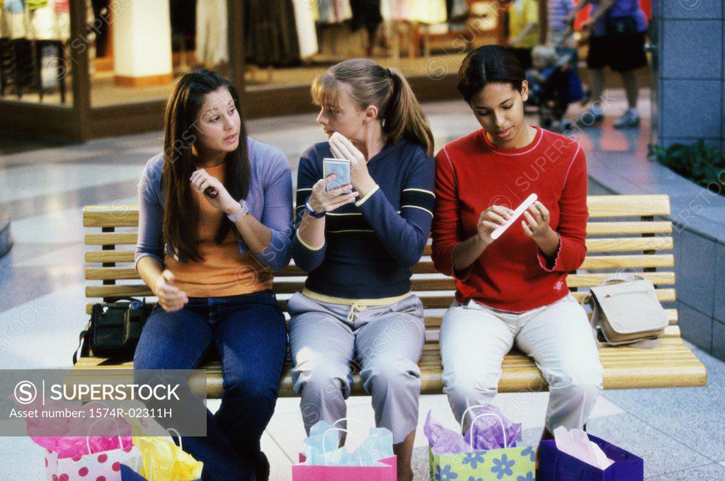 Stock Photo: 1574R-02311H Three teenage girls sitting on a bench in a shopping mall applying make-up