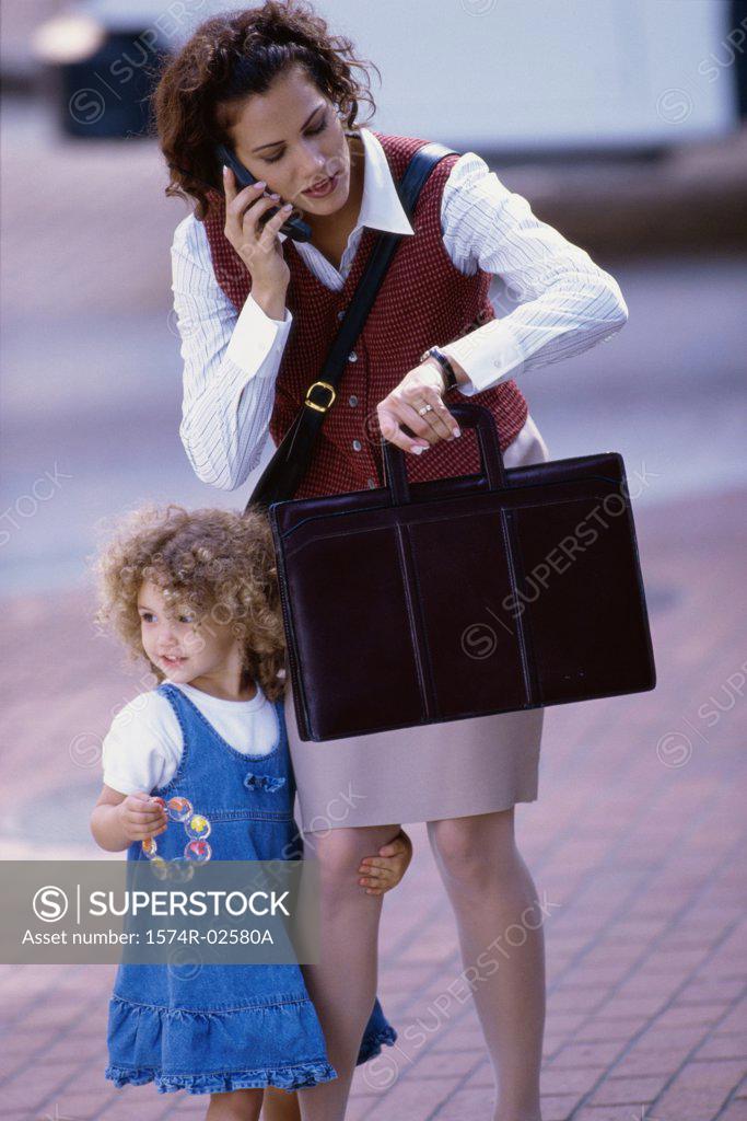 Stock Photo: 1574R-02580A Mother talking on a mobile phone with her daughter standing beside her