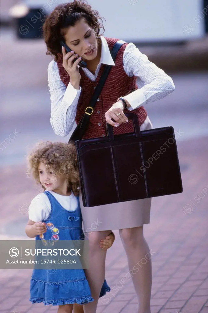 Mother talking on a mobile phone with her daughter standing beside her