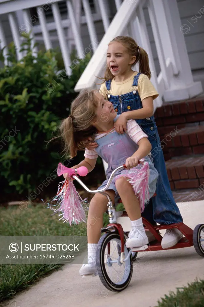 Two girls playing on a tricycle