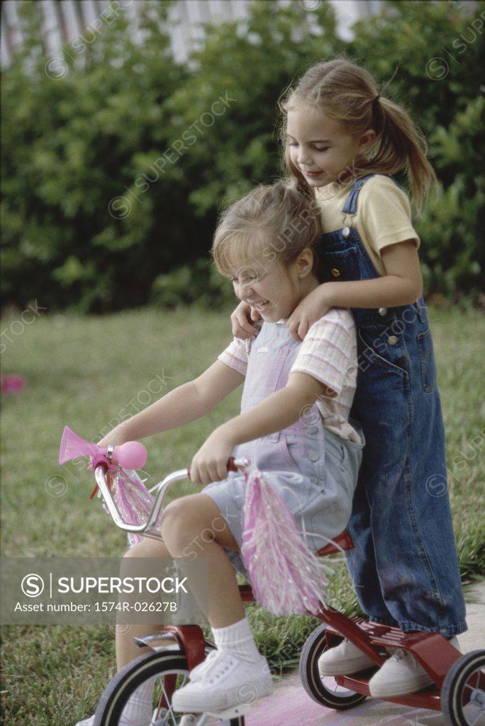Stock Photo: 1574R-02627B Side profile of two girls playing on a tricycle