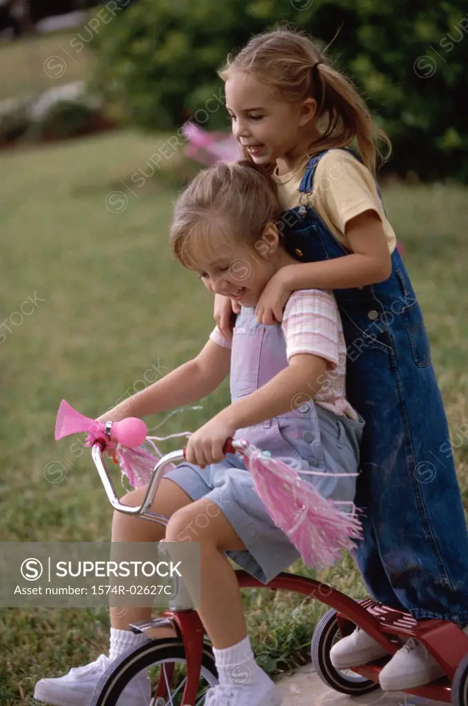 Side profile of two girls playing on a tricycle