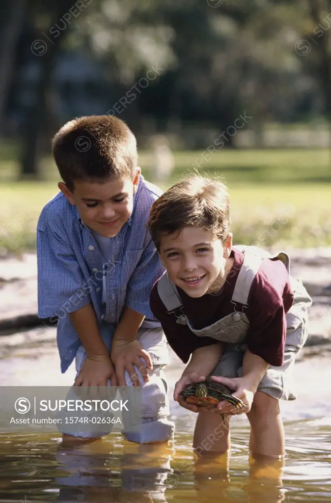 Portrait of two boys standing in water holding a turtle
