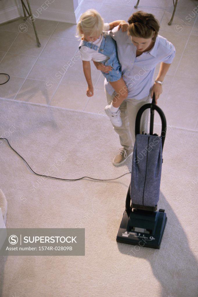 Stock Photo: 1574R-02809B High angle view of a mother vacuuming a rug and carrying her daughter