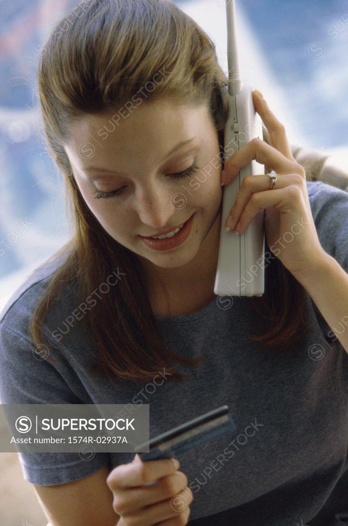 Stock Photo: 1574R-02937A Young woman using a cordless phone holding a credit card