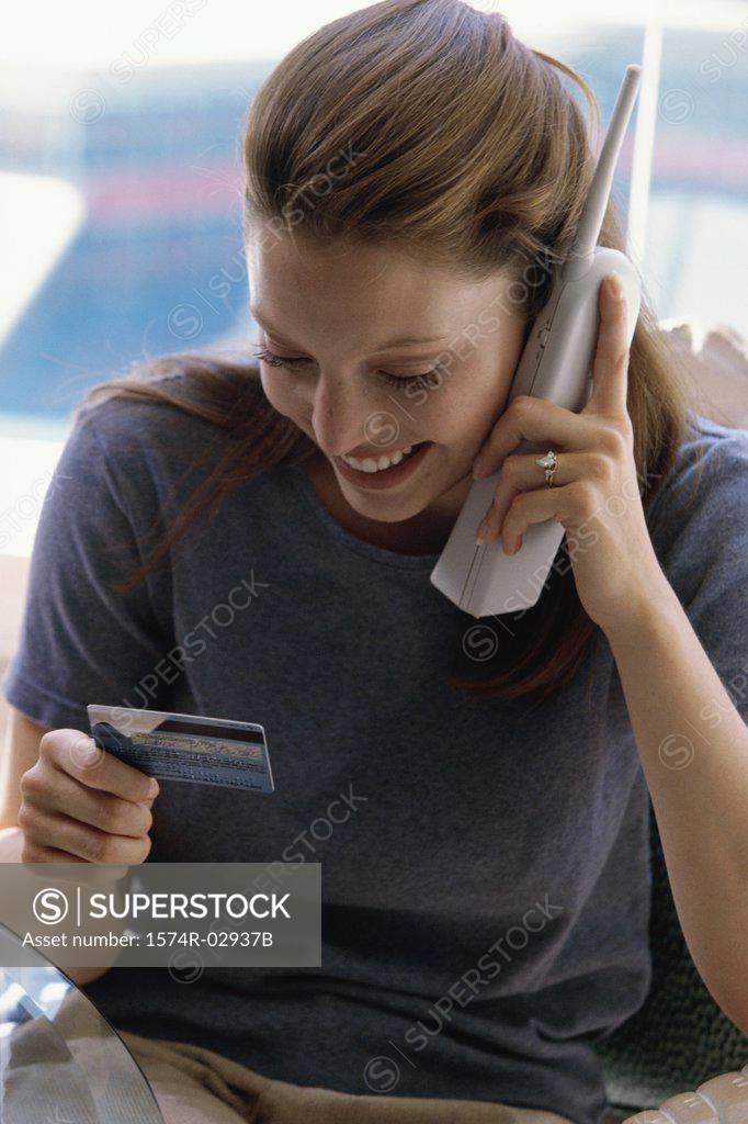 Stock Photo: 1574R-02937B Young woman using a cordless phone holding a credit card