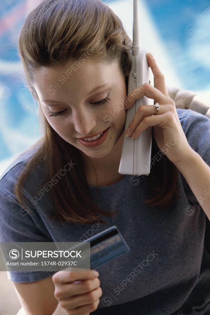 Stock Photo: 1574R-02937C Young woman using a cordless phone holding a credit card