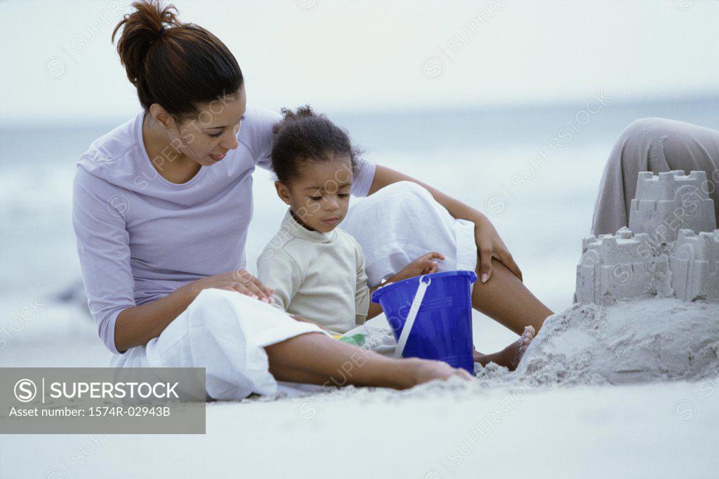Stock Photo: 1574R-02943B Woman sitting on a beach with her daughter building a sandcastle