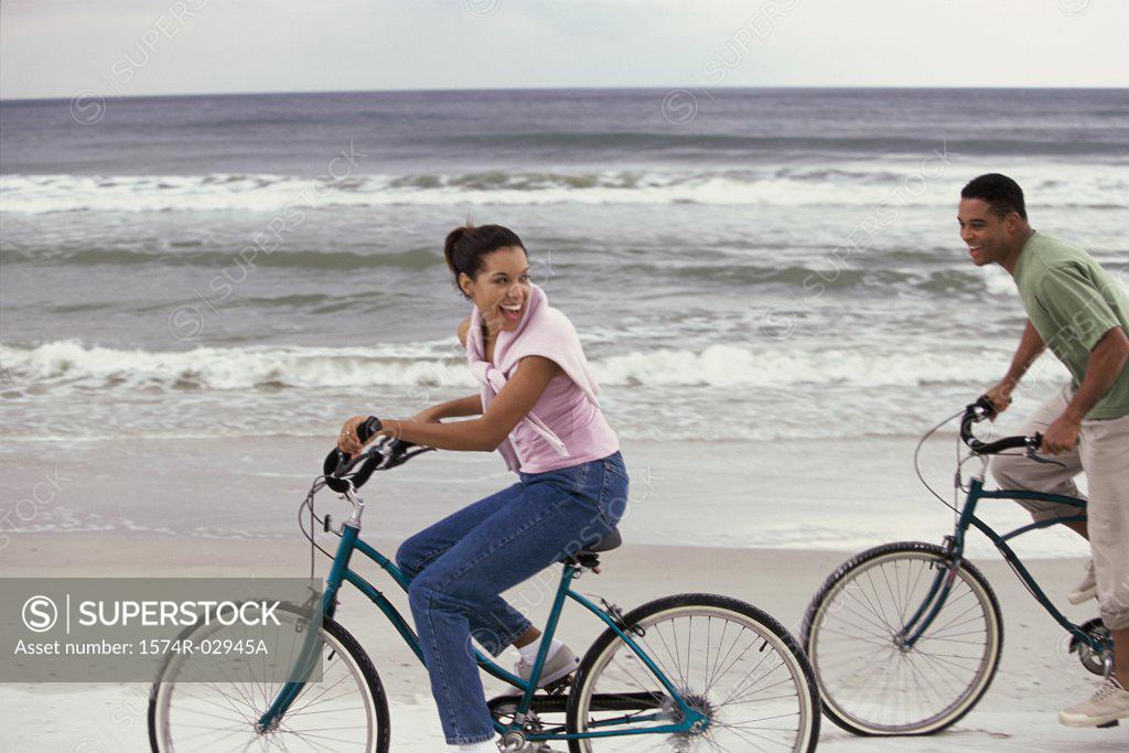 Stock Photo: 1574R-02945A Side profile of a young couple cycling on the beach