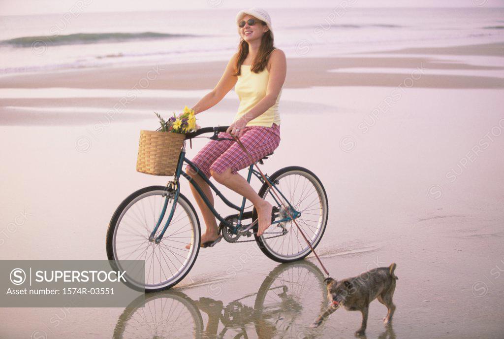 Stock Photo: 1574R-03551 Young woman riding a bicycle with her dog running alongside