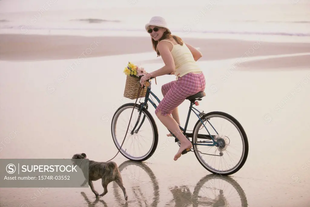 Portrait of a young woman riding a bicycle with her dog running alongside