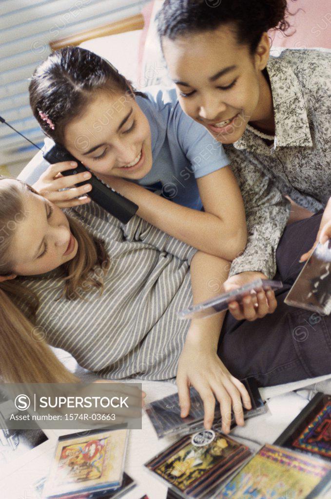 Stock Photo: 1574R-03663 Three teenage girls looking at CDs while talking on a cordless phone