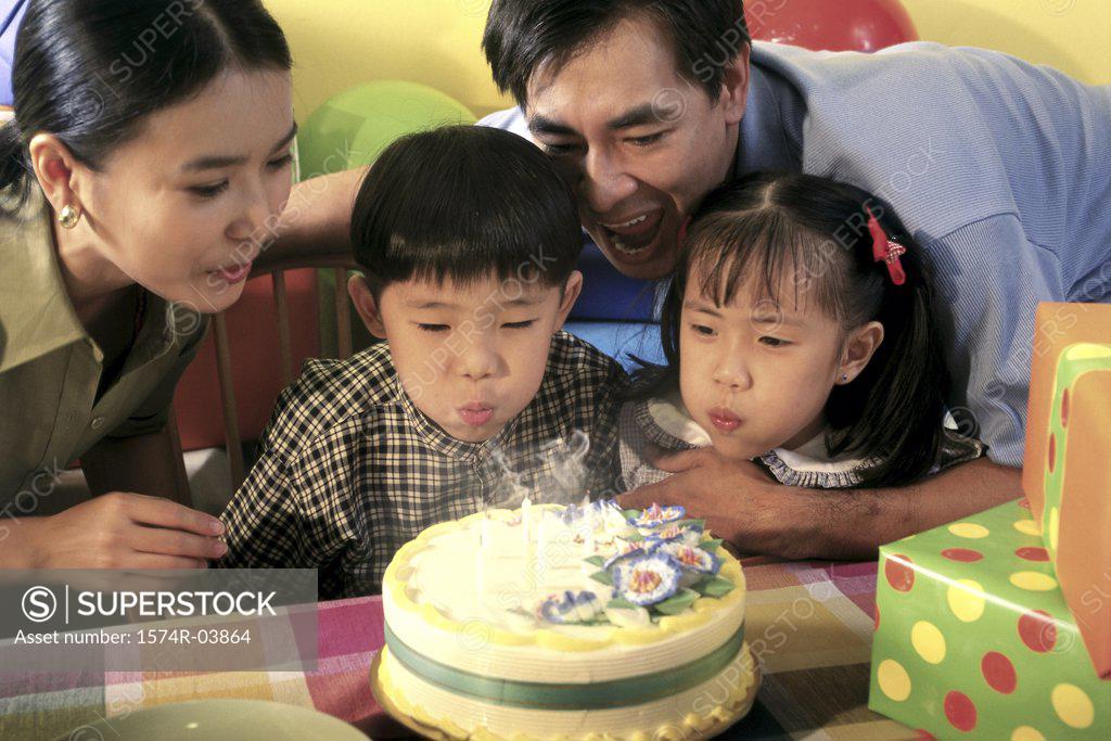 Stock Photo: 1574R-03864 Son and daughter blowing out candles on their birthday cake with their parents behind them