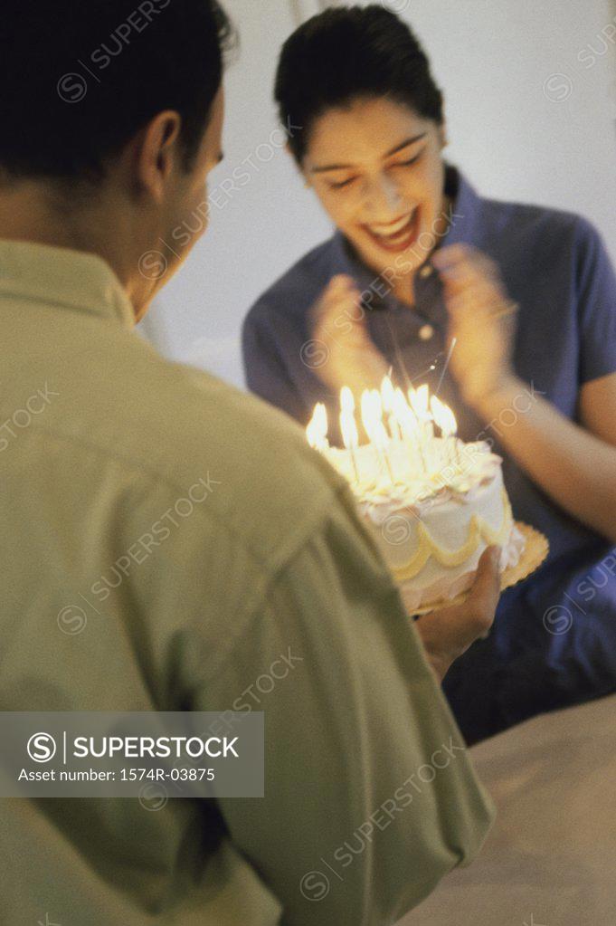Stock Photo: 1574R-03875 Mid adult man holding a birthday cake in front of a mid adult woman