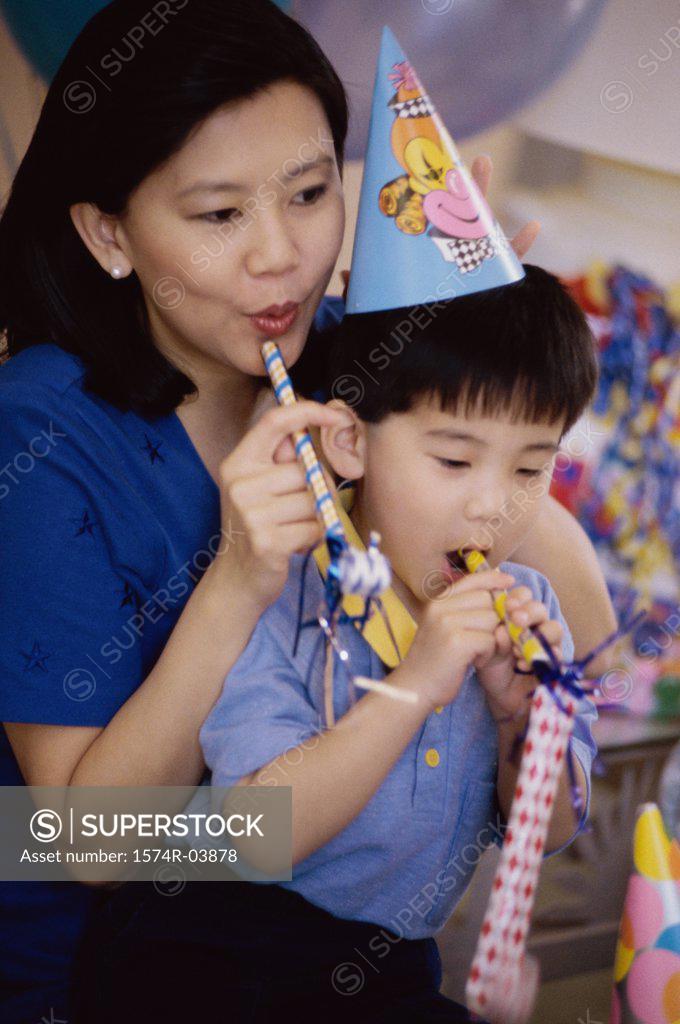 Stock Photo: 1574R-03878 Boy wearing a birthday cap blowing a party horn blower with his mother