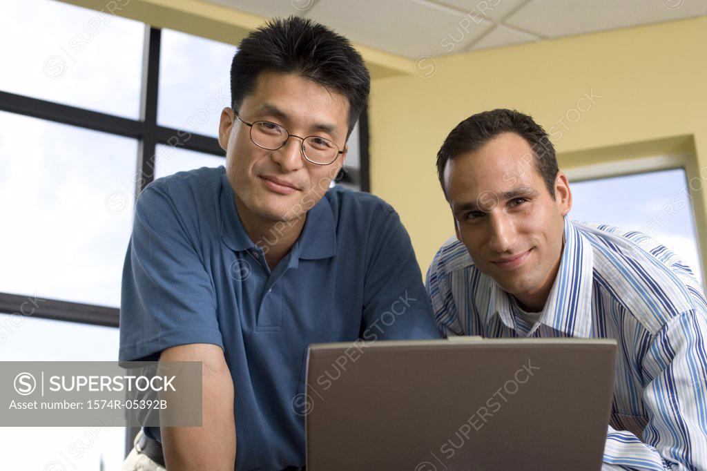 Stock Photo: 1574R-05392B Portrait of two businessmen standing in front of a laptop in an office